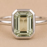close up of Sterling Silver ring with a emerald-cut, bezel set green amethyst gemstone on a beige background