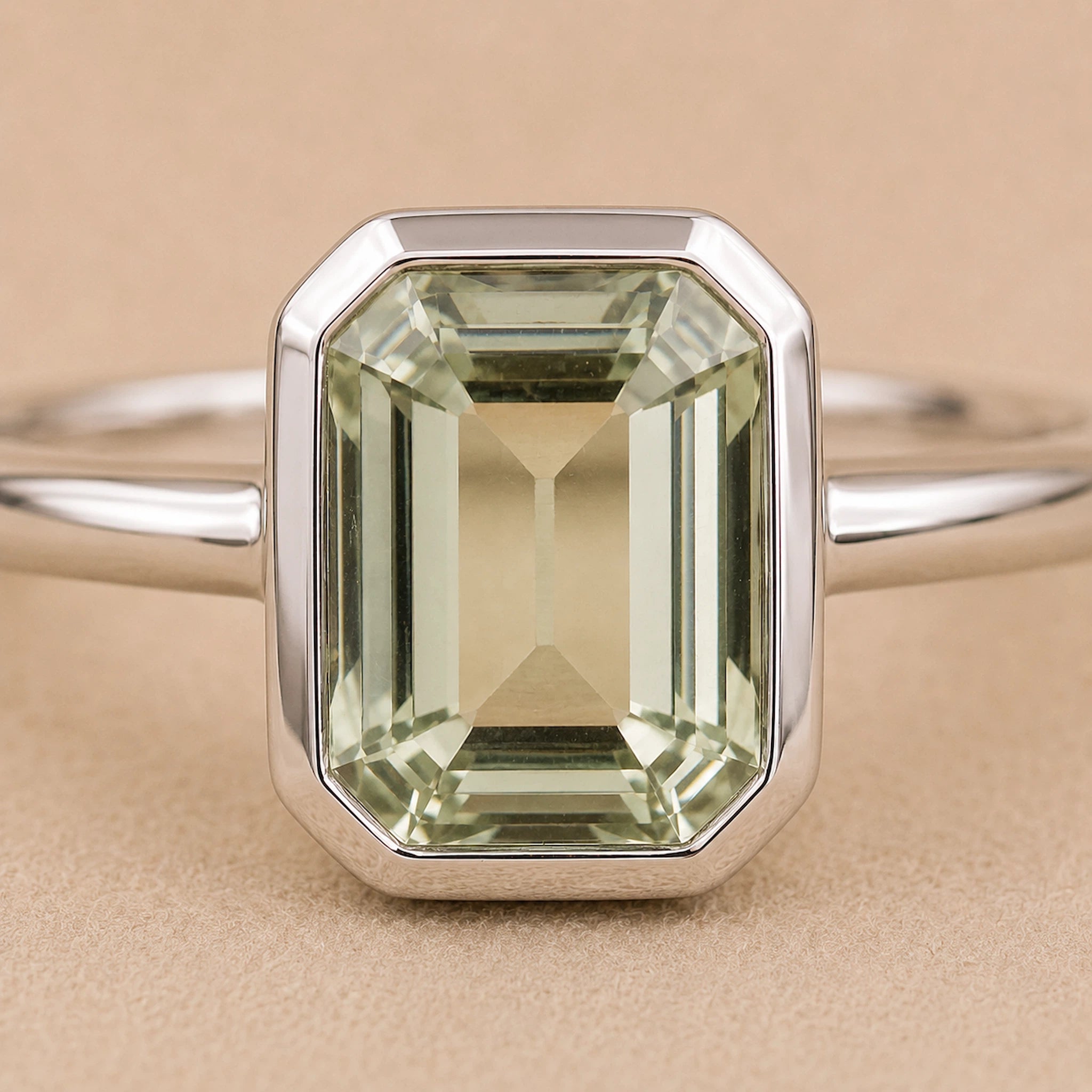 close up of Sterling Silver ring with a emerald-cut, bezel set green amethyst gemstone on a beige background