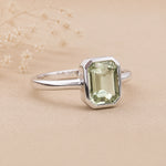 side shot of a Sterling Silver ring with a emerald-cut, bezel set green amethyst gemstone on a beige background