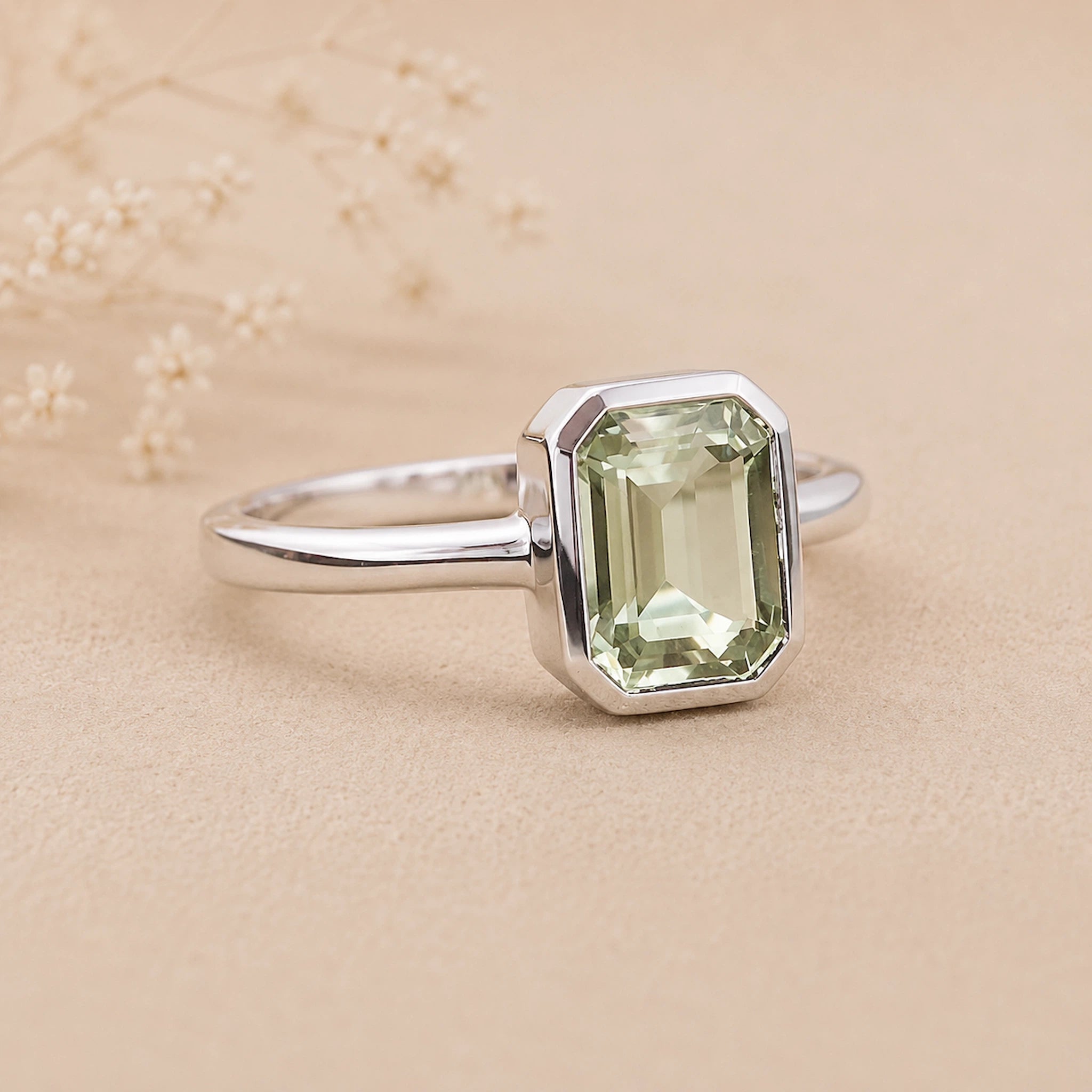 side shot of a Sterling Silver ring with a emerald-cut, bezel set green amethyst gemstone on a beige background