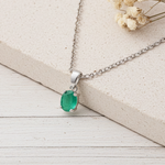 Silver necklace with an emerald pendant on a light wooden surface.