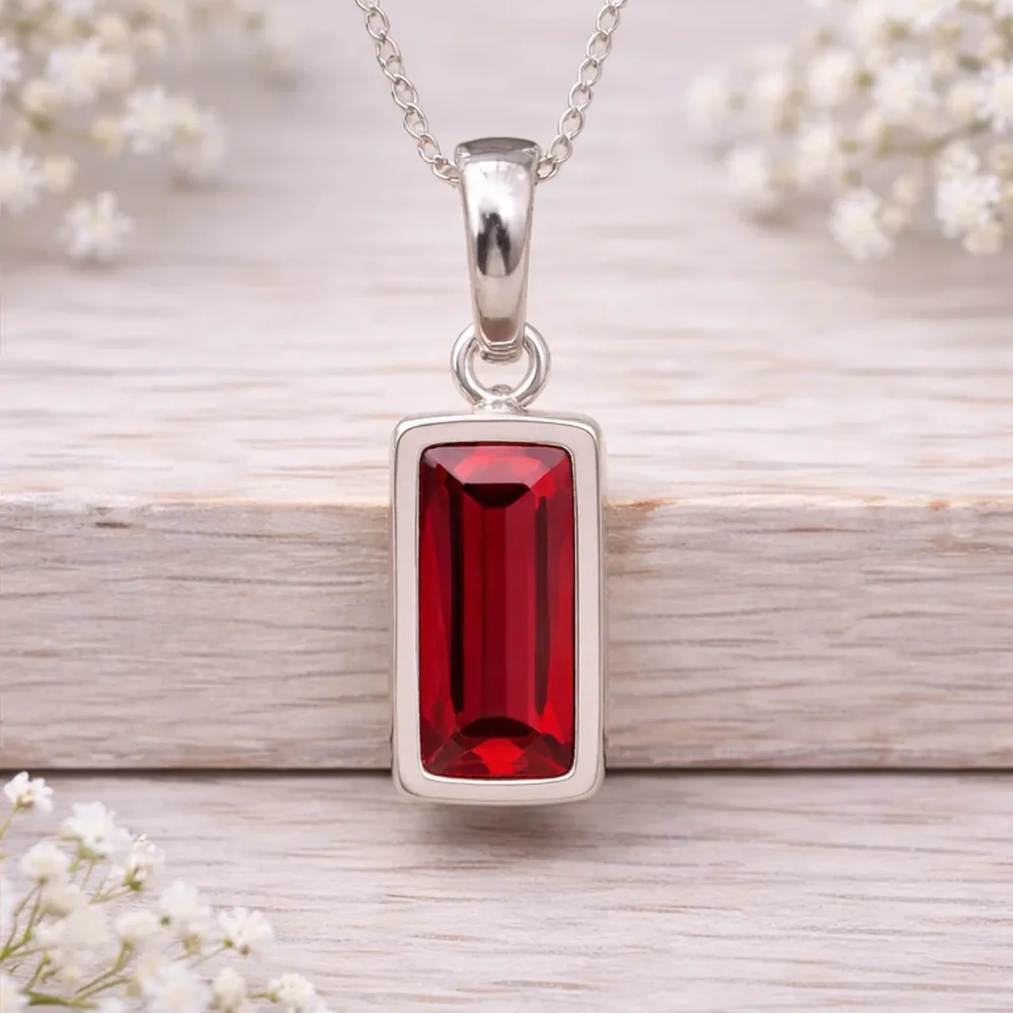 Silver waterproof necklace pendant with a red gemstone on a wooden surface with white flowers.