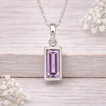 Silver waterproof necklace pendant with a pink gemstone on a wooden surface with white flowers.