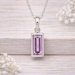 Silver pendant with a pink gemstone on a wooden surface with white flowers.