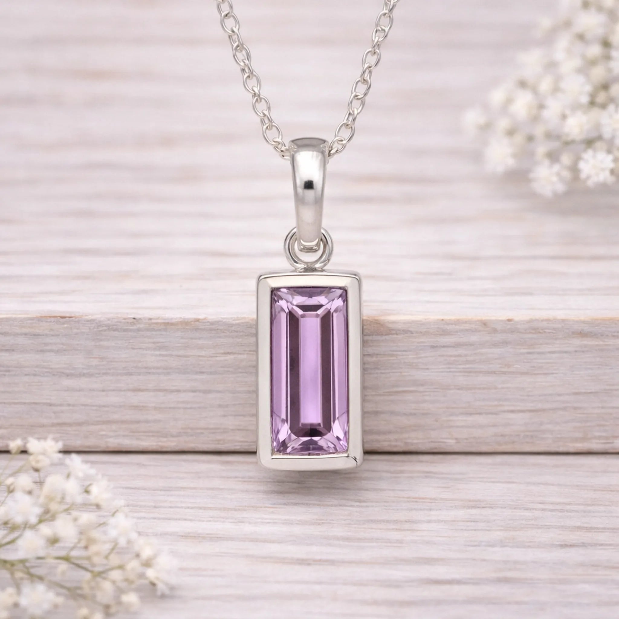 Silver pendant with a pink gemstone on a wooden surface with white flowers.