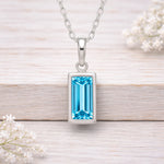 Silver waterproof necklace with a blue gemstone pendant on a light wooden surface.
