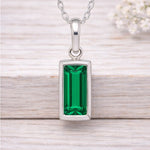 Silver waterproof necklace with a green gemstone pendant on a wooden surface
