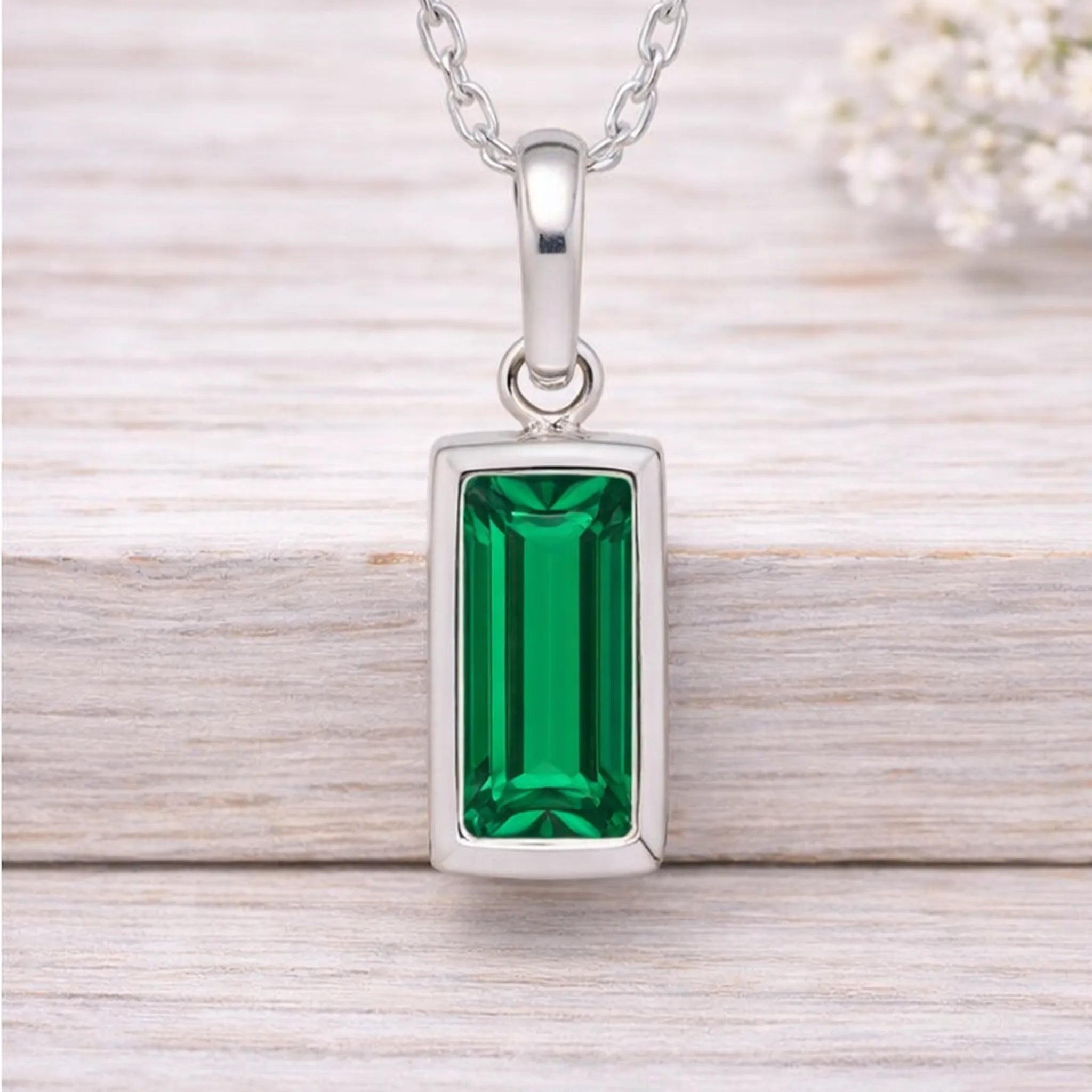 Silver waterproof necklace with a green gemstone pendant on a wooden surface