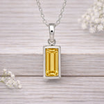 Silver pendant with a yellow gemstone on a wooden surface with white flowers.