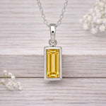 Silver waterproof necklace pendant with a yellow gemstone on a wooden surface with white flowers.