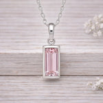 Silver waterproof necklace pendant with a pink gemstone on a wooden surface