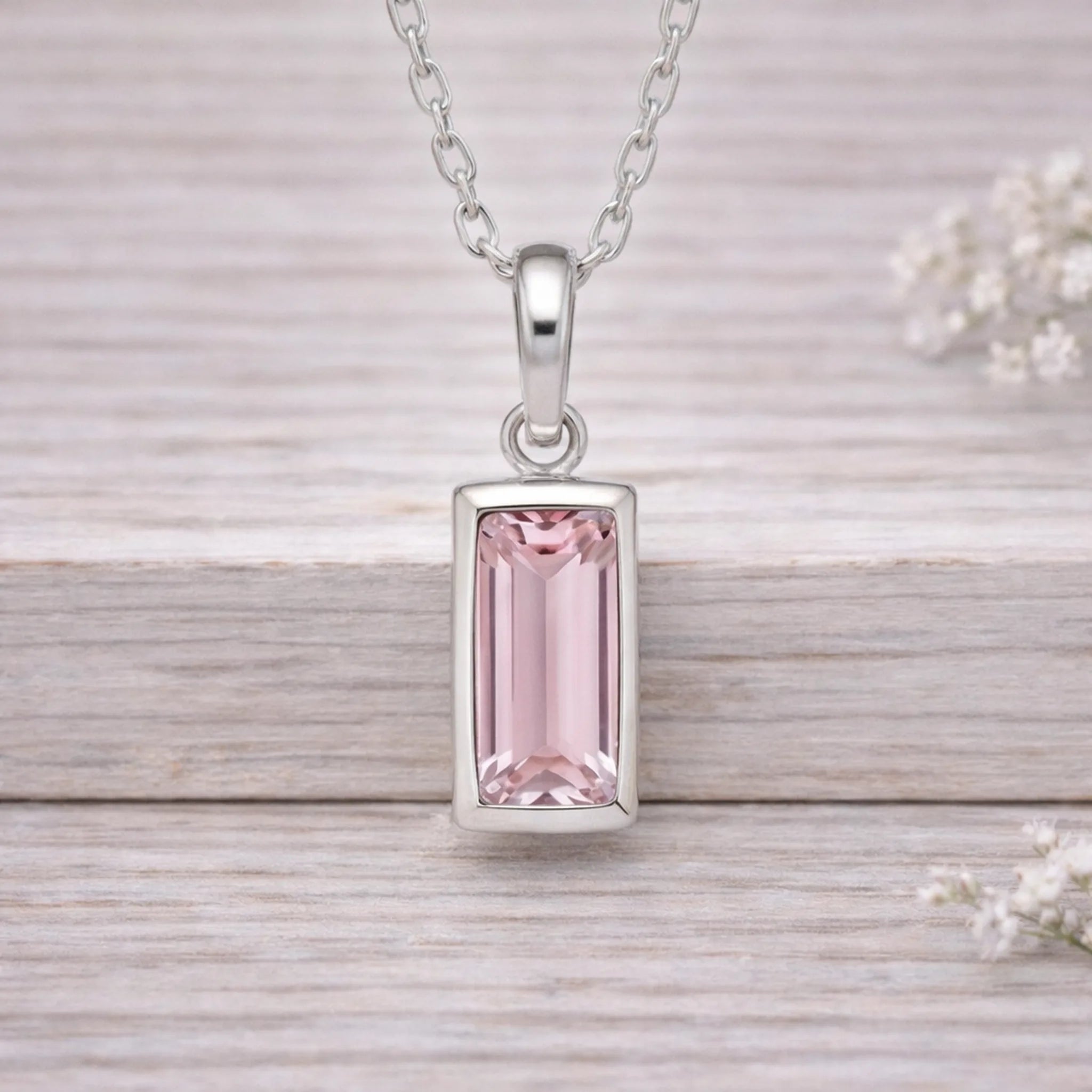 Silver waterproof necklace pendant with a pink gemstone on a wooden surface