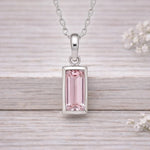 Silver pendant with a pink gemstone on a wooden surface
