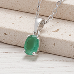 Silver necklace with a green emerald gemstone pendant on a wooden surface