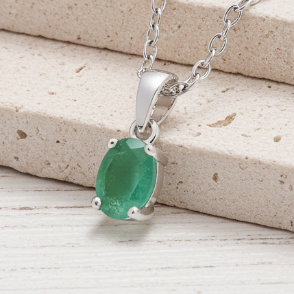 Silver necklace with a green emerald gemstone pendant on a wooden surface
