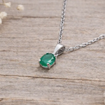 Silver necklace with a green pendant on a light wooden surface with dried flowers.