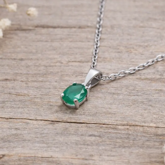 Silver necklace with a green pendant on a light wooden surface with dried flowers.