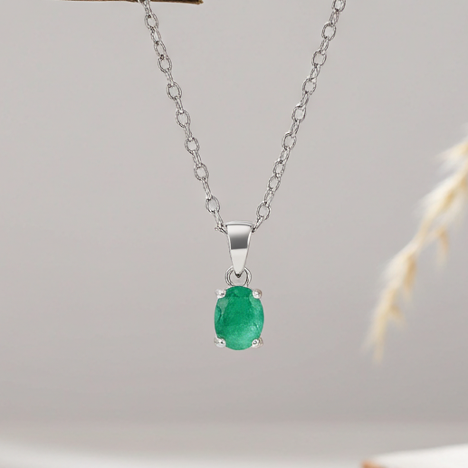 Silver necklace with a green emerald gemstone pendant on a light gray background