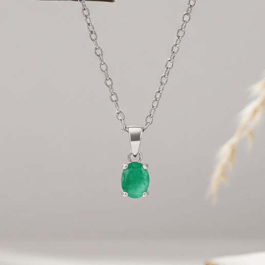 Silver necklace with a green emerald gemstone pendant on a light gray background