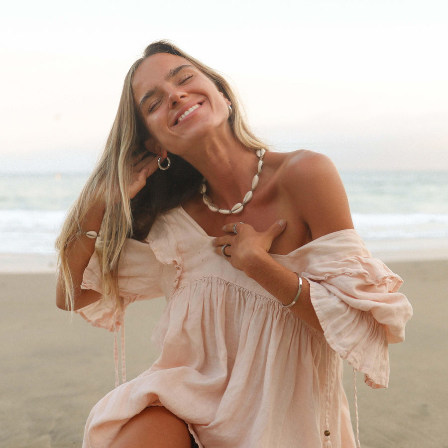 Woman on beach smiling wearing cowrie sea shell jewellery - Australian jewellery brand