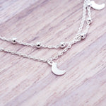 Silver layered anklet with moon pendants on a wooden surface