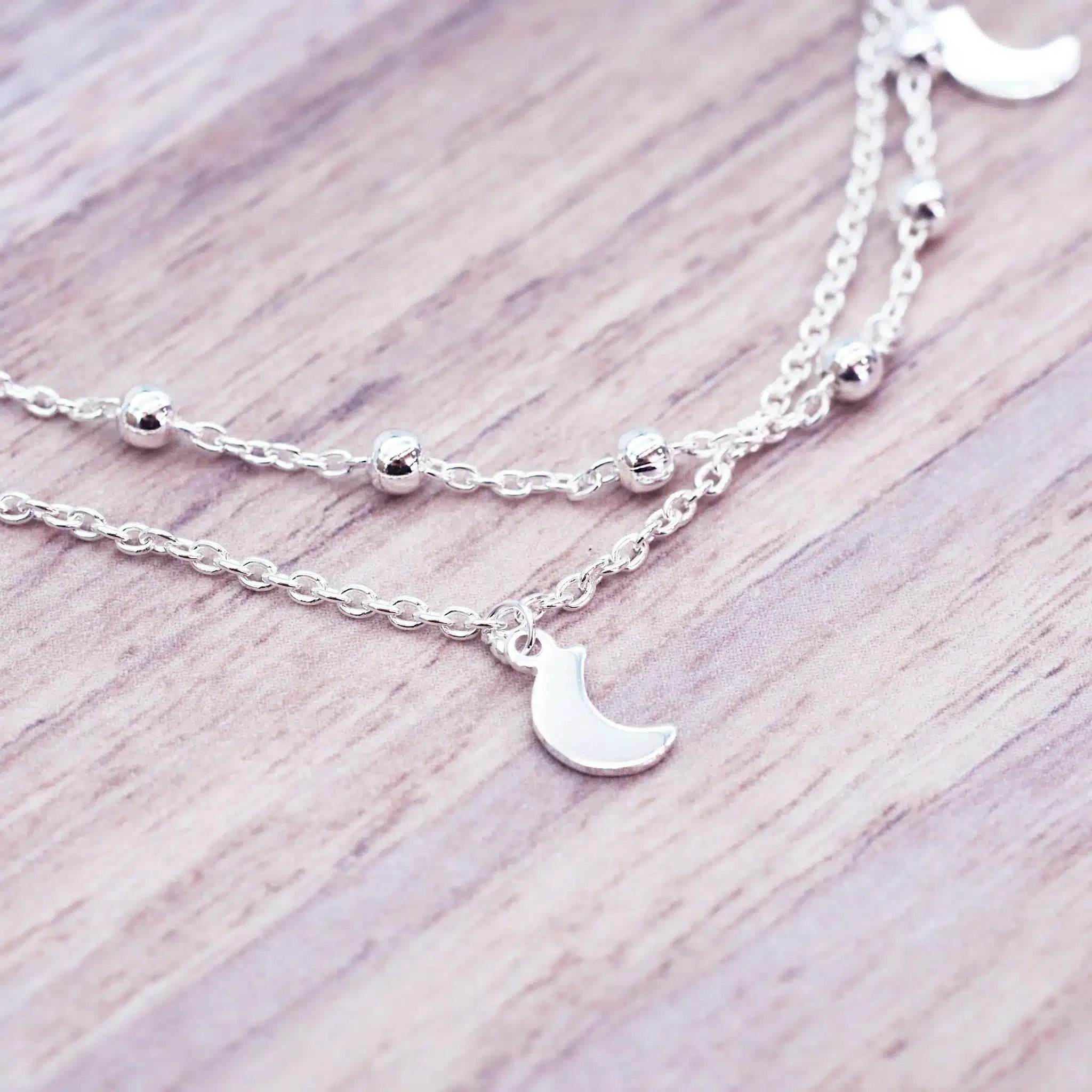 Silver layered anklet with moon pendants on a wooden surface