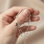 Hand holding silver anklet with moon pendants on a neutral background
