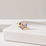 A gold post piercing stud featuring three marquise-cut iridescent crystals, displayed on a clean white geometric block against a neutral light gray background.