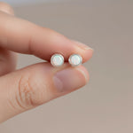 Opal stud earrings held between two fingers against a neutral background