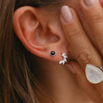 Close-up of an ear with black only gemstone stud earring and white floral earrings, hand holding the ear.