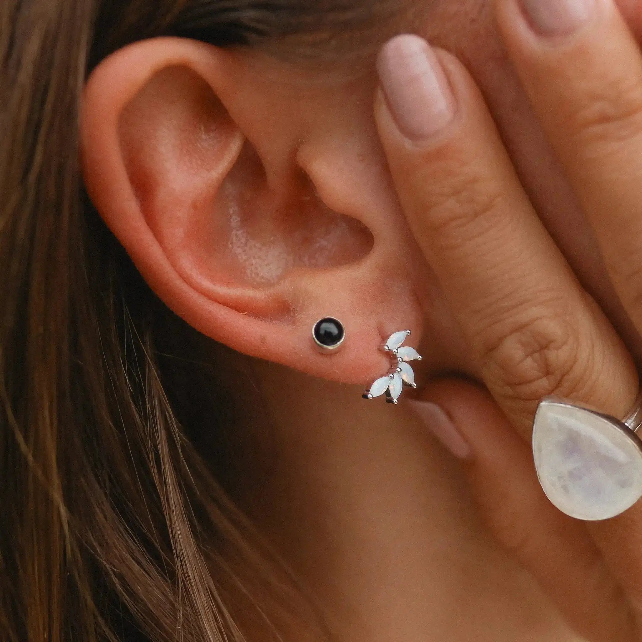 Close-up of an ear with black only gemstone stud earring and white floral earrings, hand holding the ear.