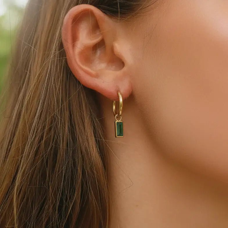 Close-up of an ear with a gold earring featuring a green gemstone