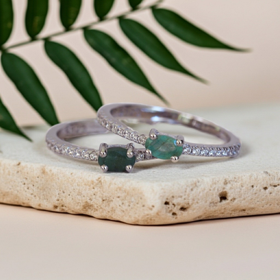 Two silver rings with green gemstones on a stone surface with leaves in the background
