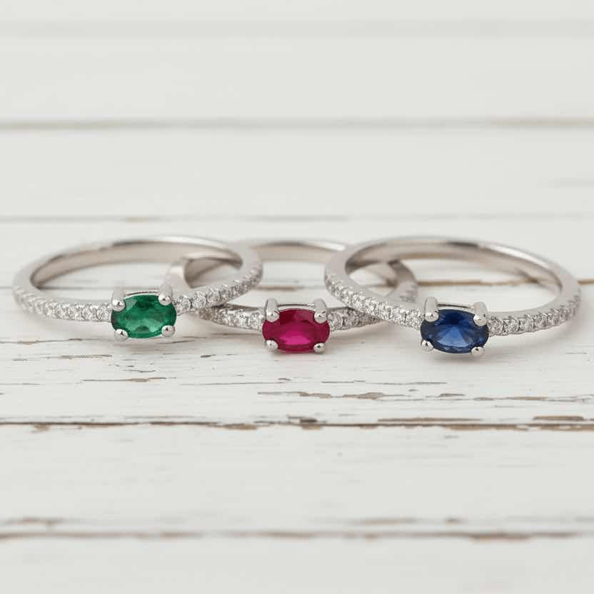 Three silver rings with colored gemstones on a wooden surface with flowers in the background