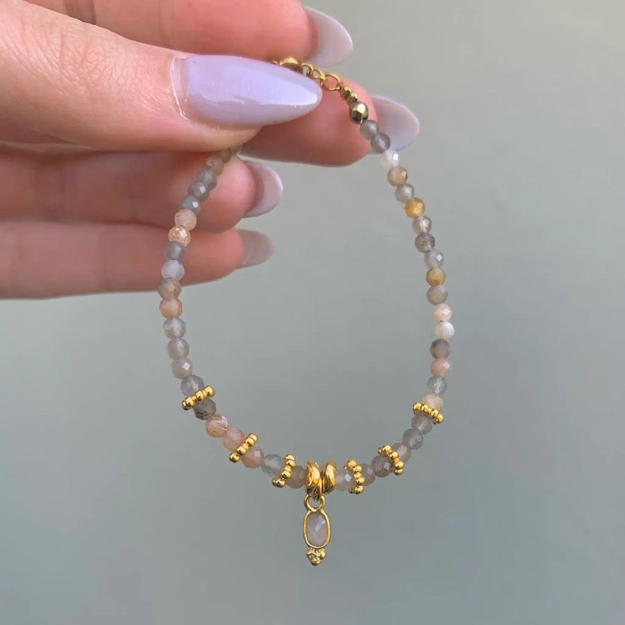 woman holding stainless steel bracelet with gold detailing and orange moonstone beads