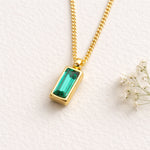 Gold necklace with a green gemstone pendant on a white background