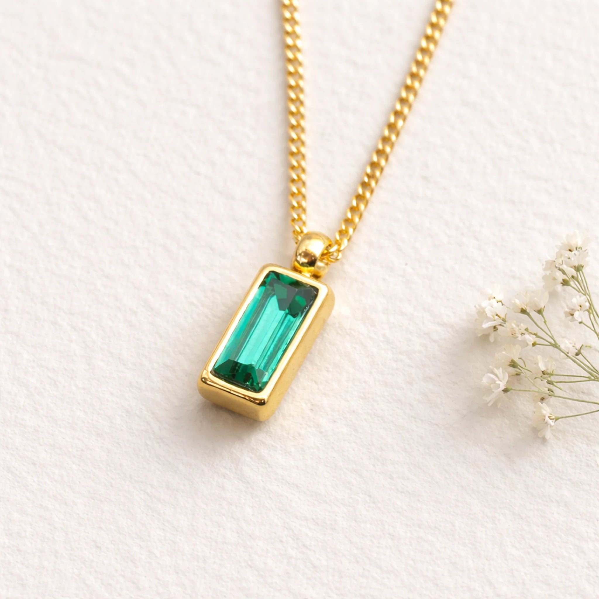 Gold necklace with a green gemstone pendant on a white background