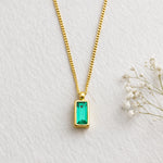Gold necklace with a green gemstone pendant on a light gray background