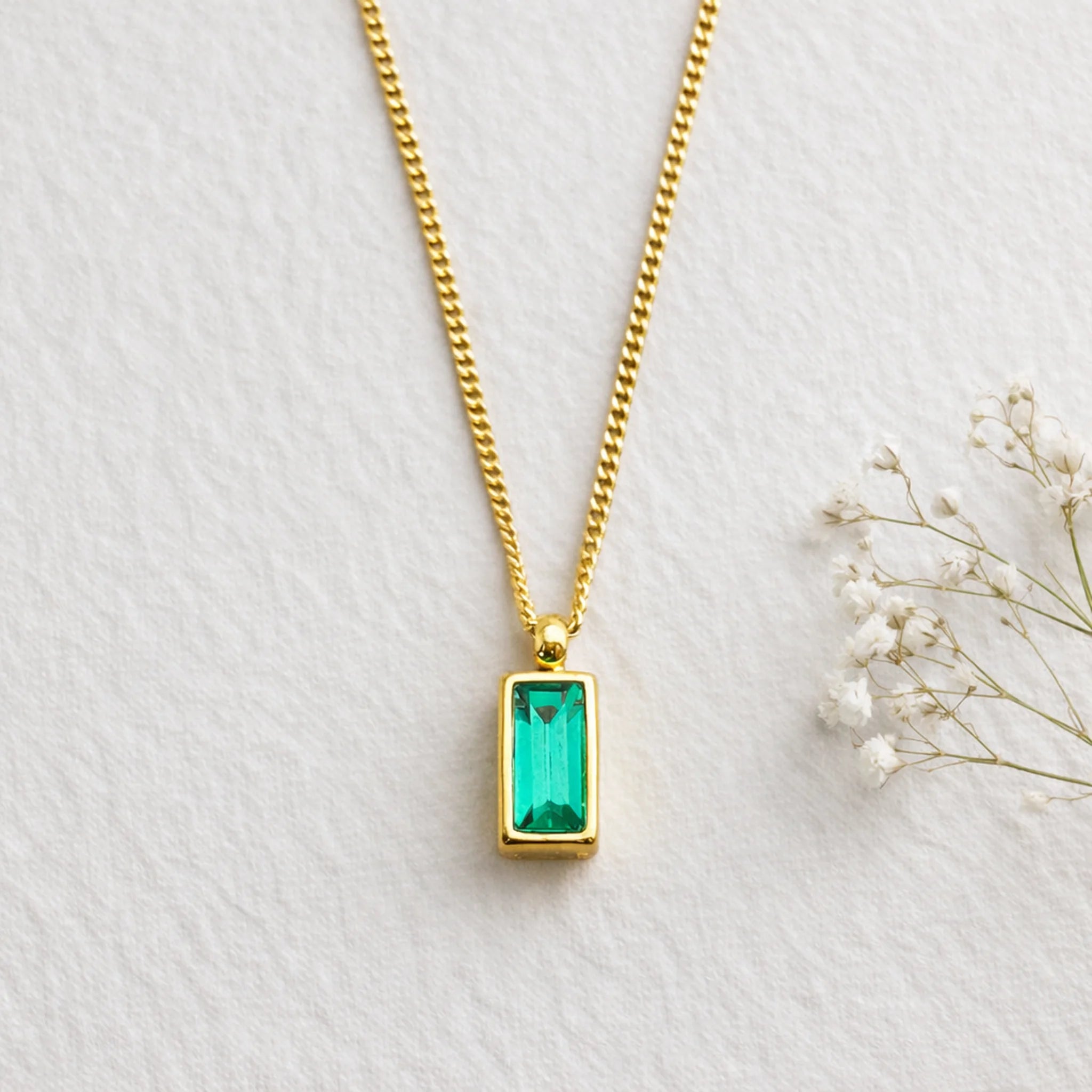 Gold necklace with a green gemstone pendant on a light gray background
