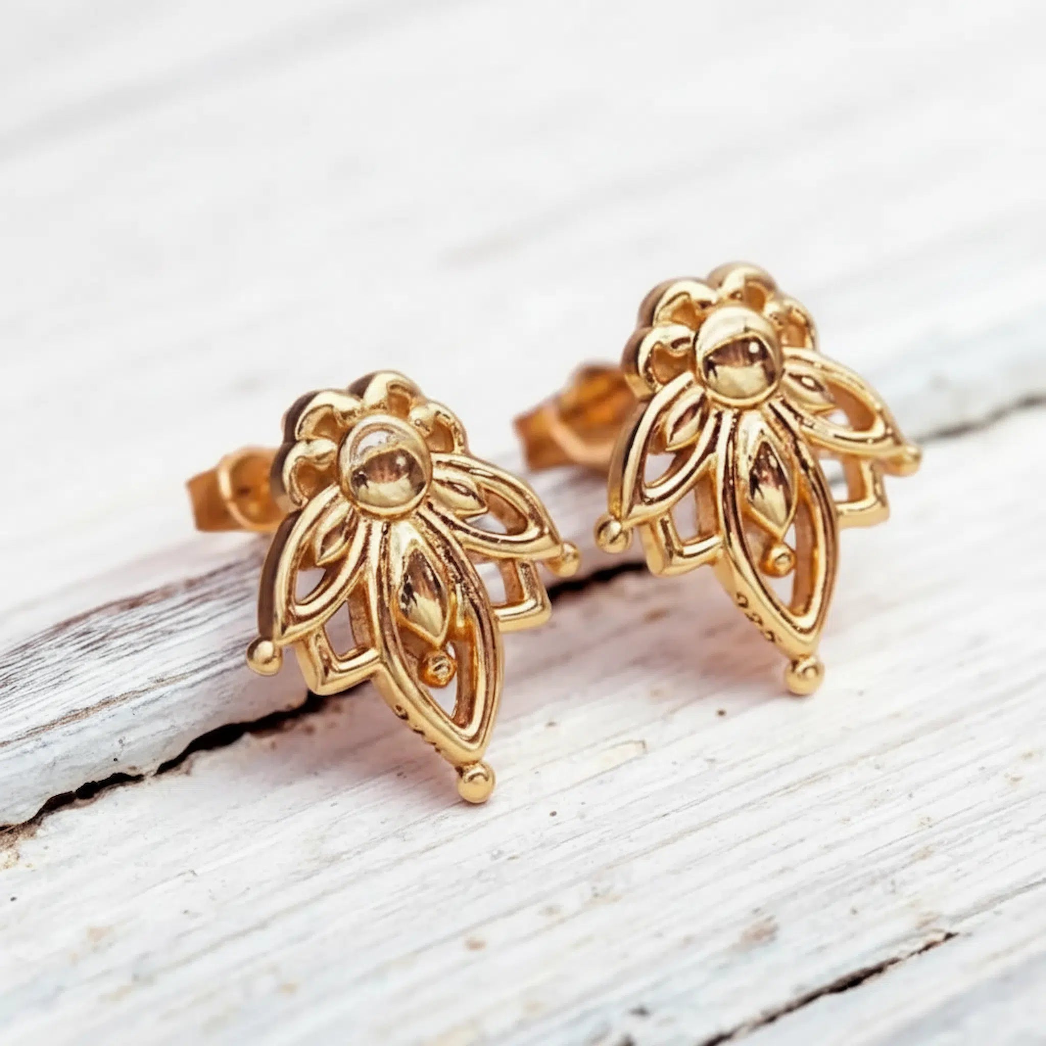gold dainty lotus flower stud earrings on a piece of wood by indie and harper australia