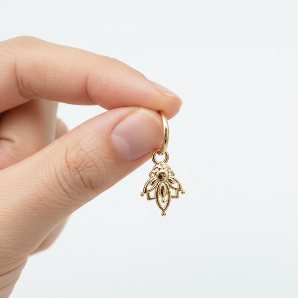Gold hoop earring with a dangling lotus charm held by a hand against a white background
