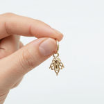 Gold hoop earring with a dangling lotus charm held by a hand against a white background