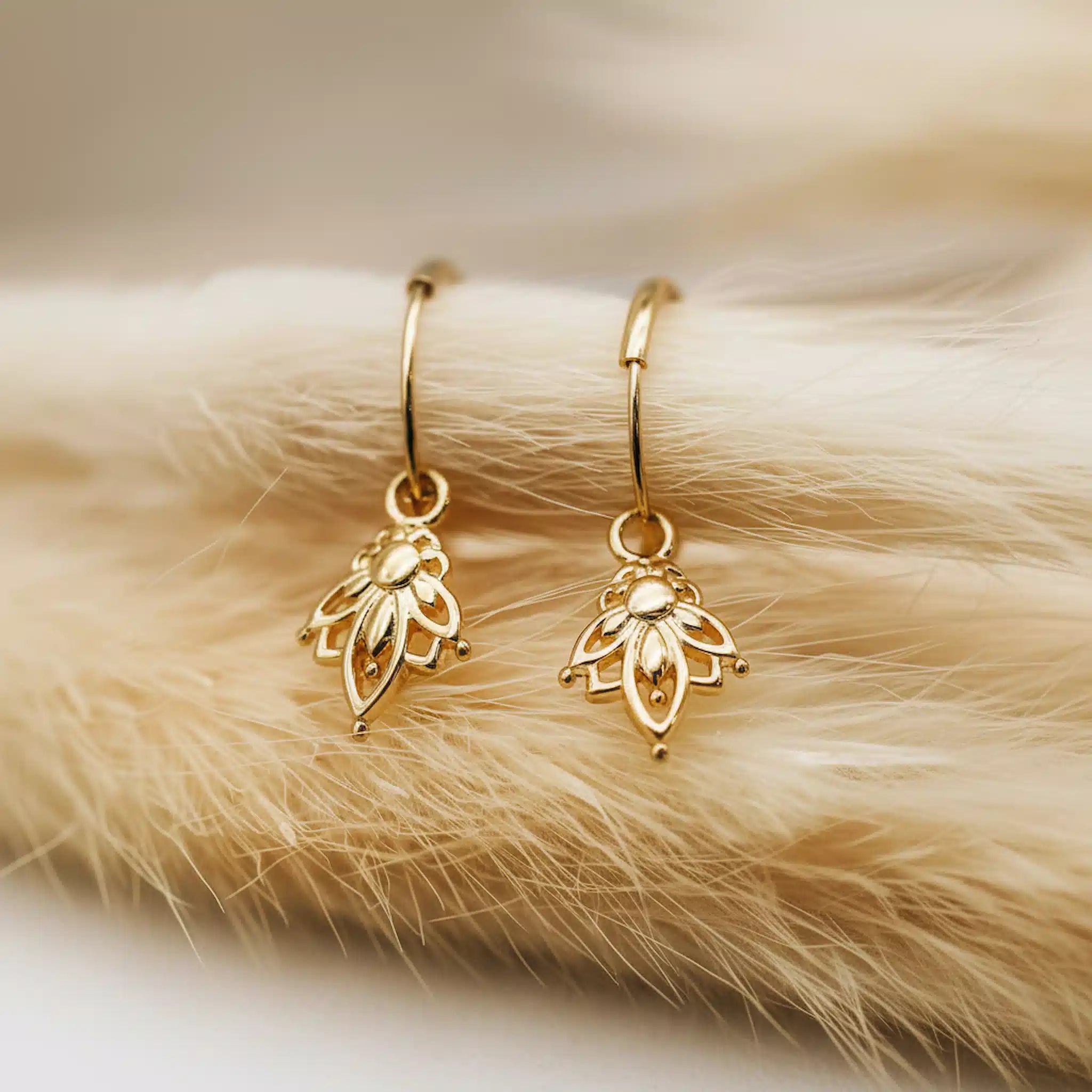 Gold lotus hoop earrings on a fur surface