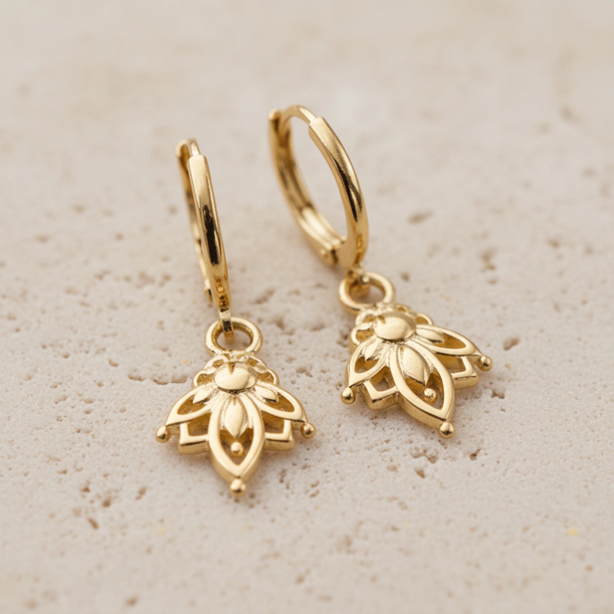 Gold hoop earrings with intricate lotus flower designs on a beige background