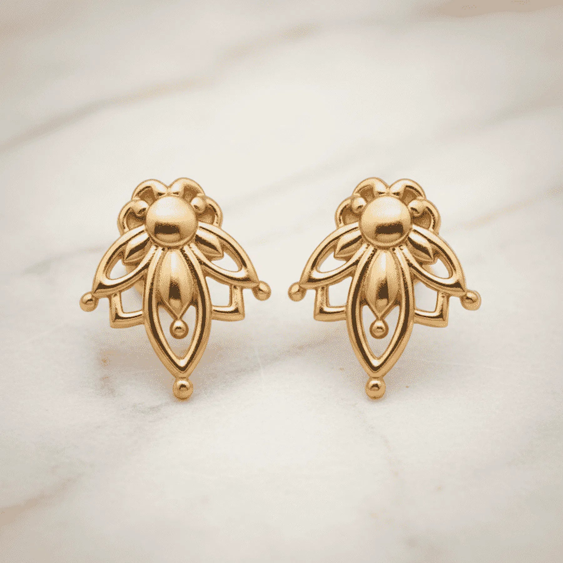 dainty gold lotus flower stud earrings on a light surface