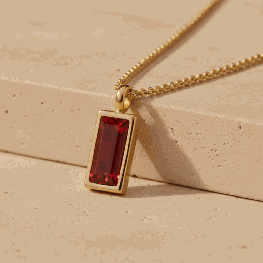 Gold necklace with a red gemstone pendant on a natural stone background