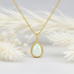 Gold necklace with a teardrop-shaped opal pendant on a white background