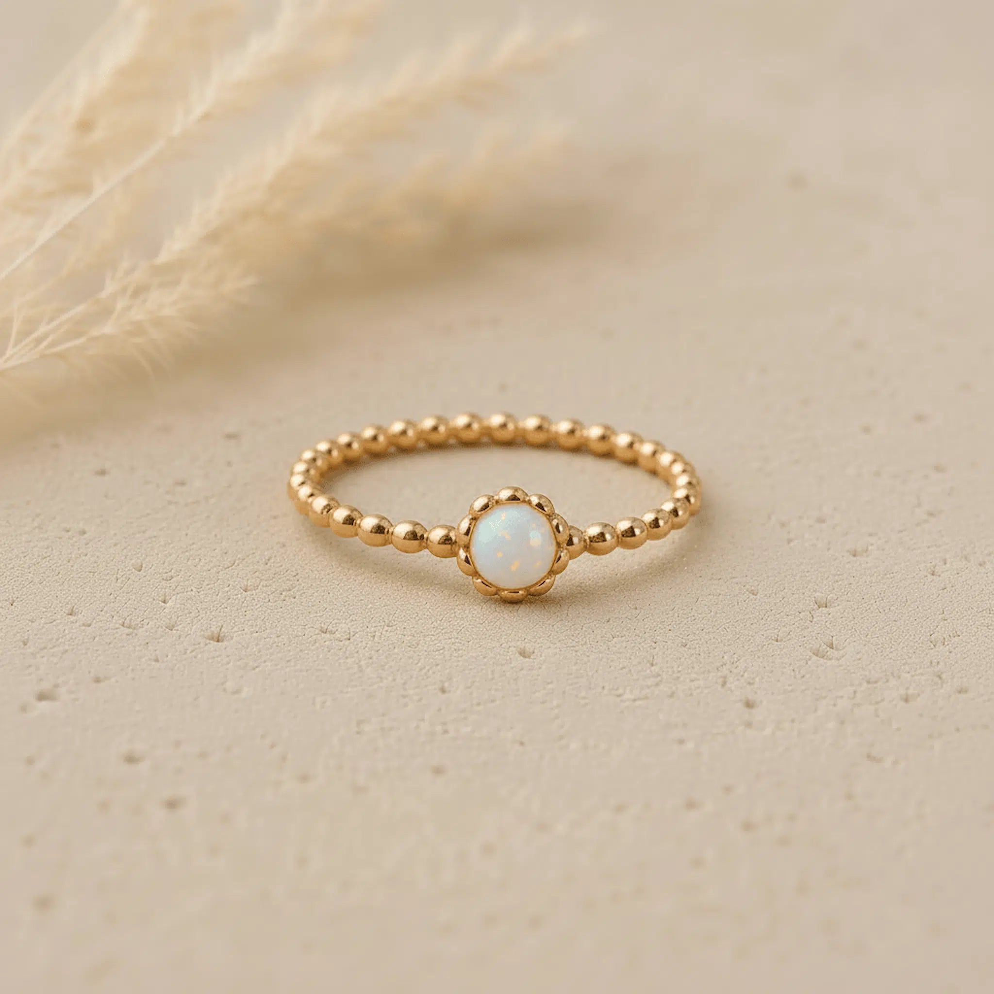 Gold ring with a lab-grown small white opal stone on a beige background