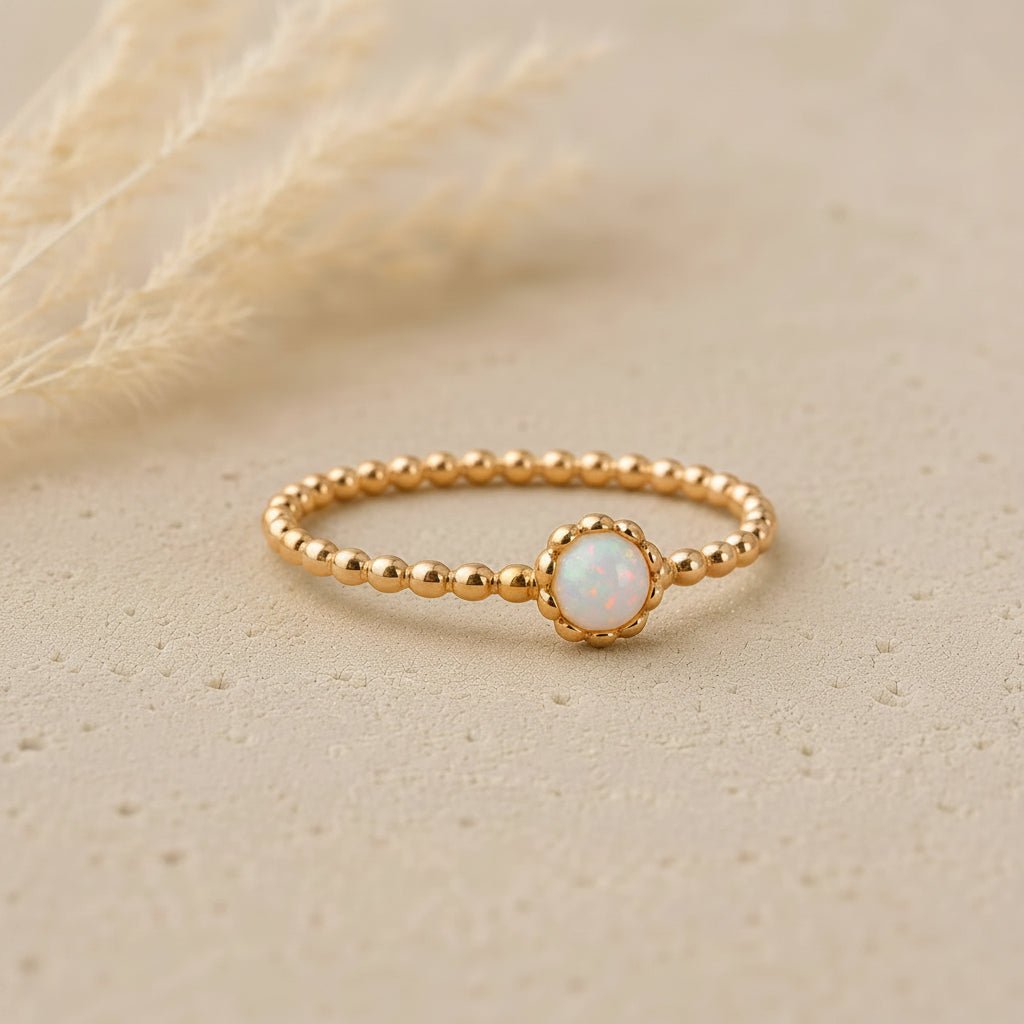 Gold ring with a small opal stone on a beige background