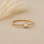 Gold ring with a small opal stone on a beige background
